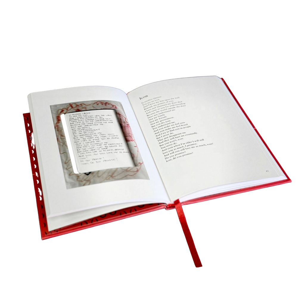 An open hardcover book with a red cover and ribbon bookmark, showing printed text pages and a small inset page or card inside the spread, isolated on a white background.
