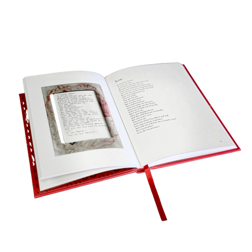 An open hardcover book with a red cover and ribbon bookmark, showing printed text pages and a small inset page or card inside the spread, isolated on a white background.