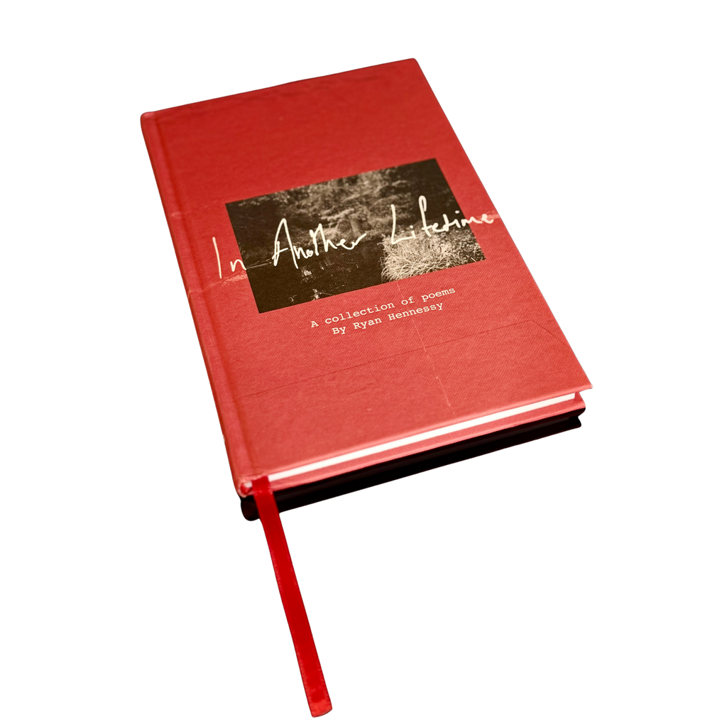 A red hardcover book titled 'In Another Lifetime: A collection of poems' by Ayan Hemasy, shown at an angle on a plain white background with a red ribbon bookmark extending from the bottom.